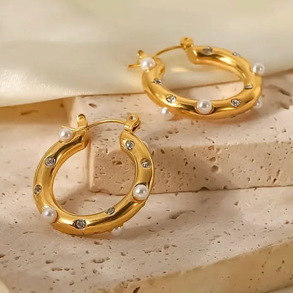 Caia Classic Studded Huggies. These exquisite earrings, crafted from 18K gold plated stainless steel, feature a dazzling array of zircon stones or pearls.