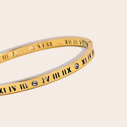 Close up of Hendrix Hinged Bangle. Crafted from stainless steel, this hinged bangle features eye-catching Roman numerals and sparkling zircon stones. In gold.