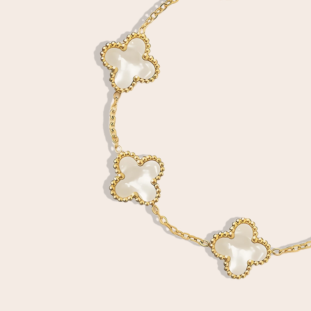 This charming piece in white features five delicate quatrefoil charms, crafted in stainless steel and lavishly plated in 18K gold. Close up.