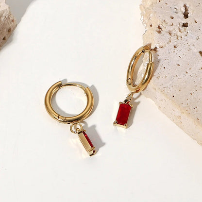 Rhea Rectangular Huggies in ruby. Made from stainless steel and plated with 18k gold, these earrings are inlaid with sparkling cubic zirconia. Lifestyle shot.