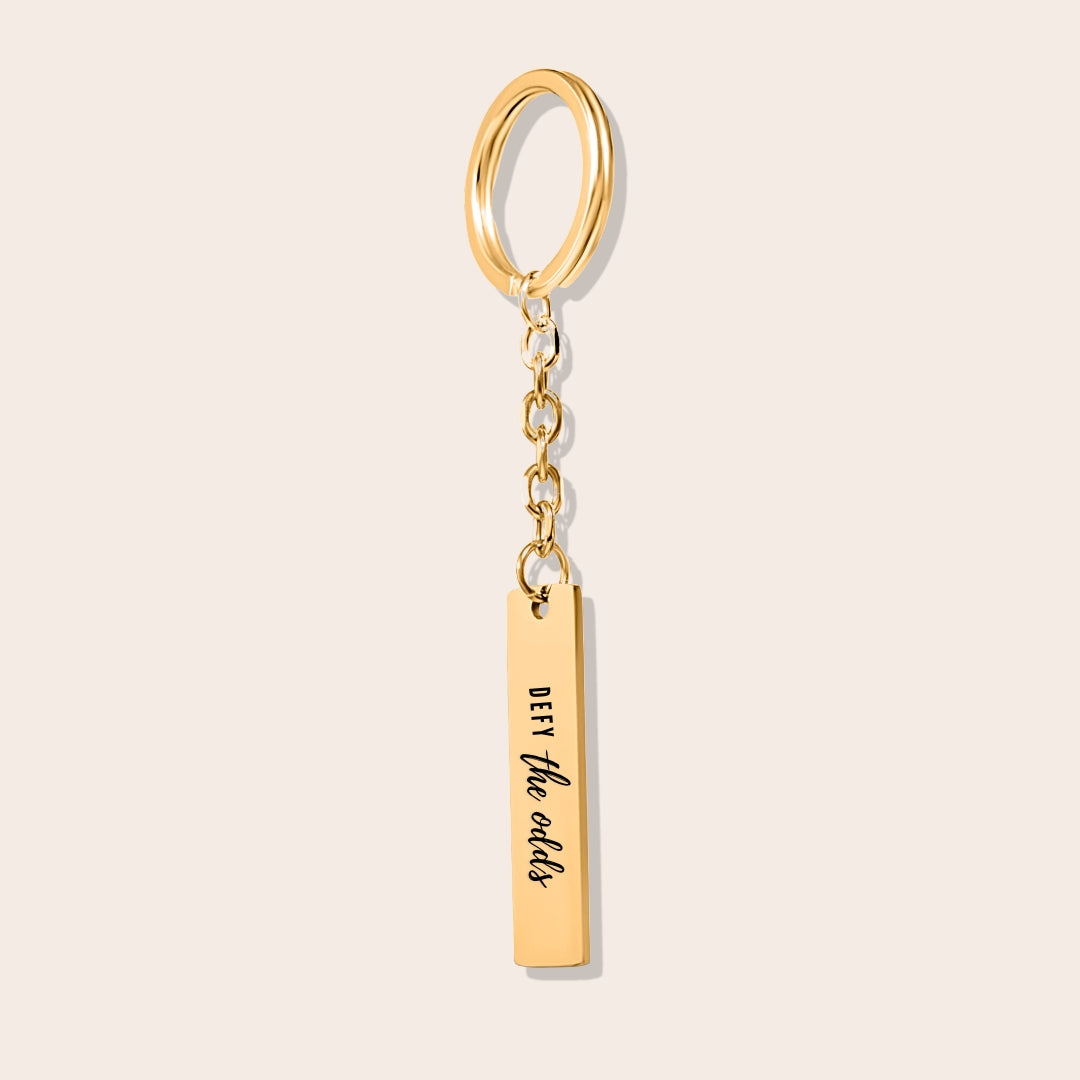 Vertical Bar Keychain - Defy the Odds in gold. Crafted from stainless steel and plated with 18K gold.