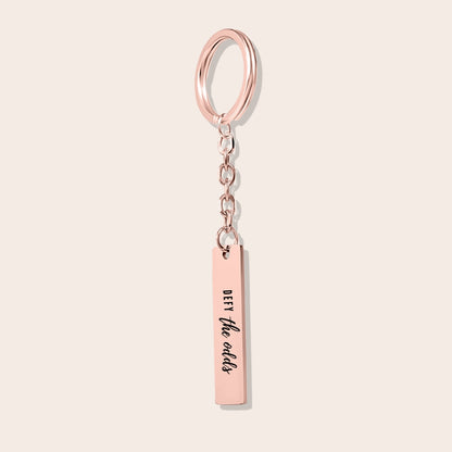 Vertical Bar Keychain - Defy the Odds in rose gold. Crafted from stainless steel and plated with 18K gold.