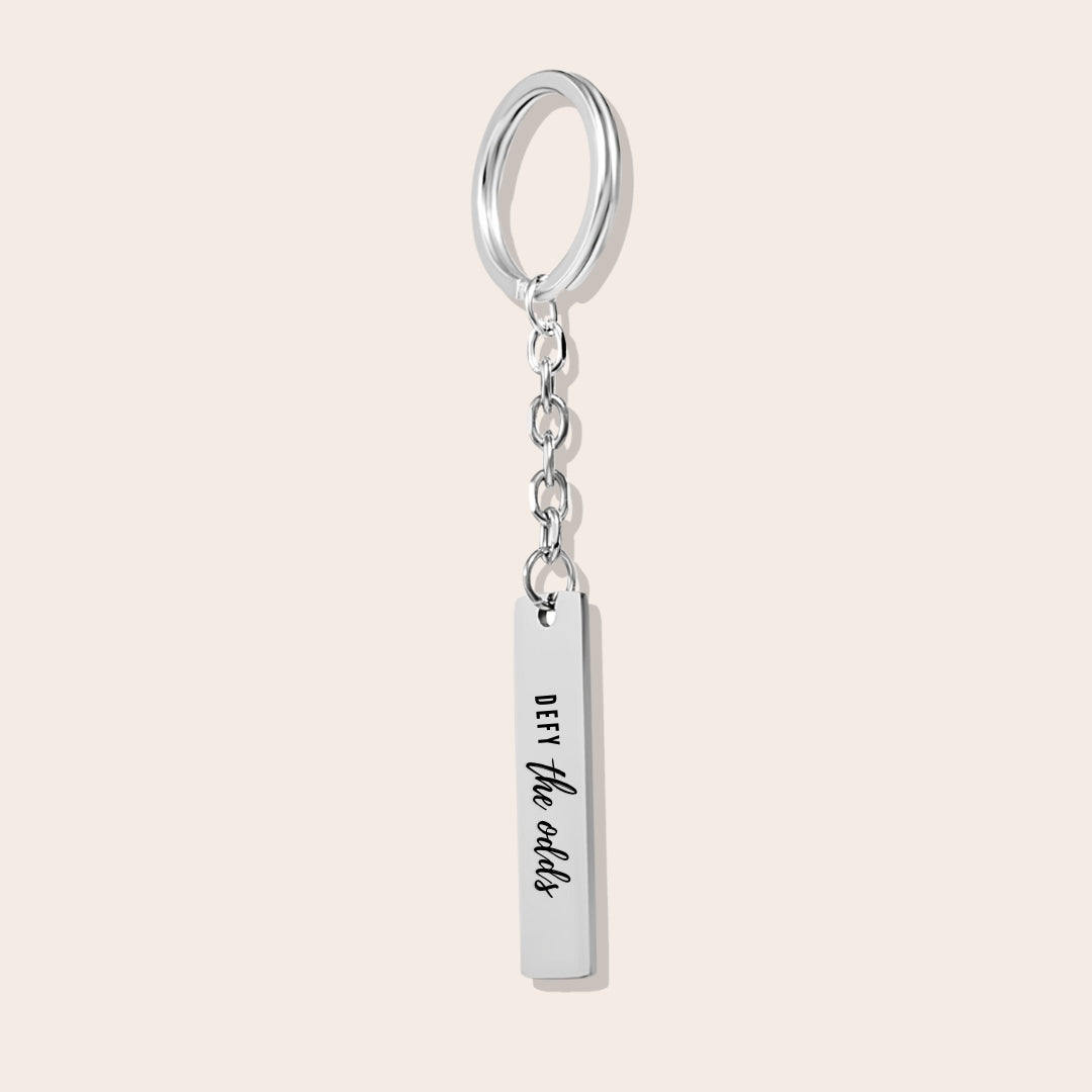 Vertical Bar Keychain - Defy the Odds in silver. Crafted from stainless steel and plated with 18K gold.