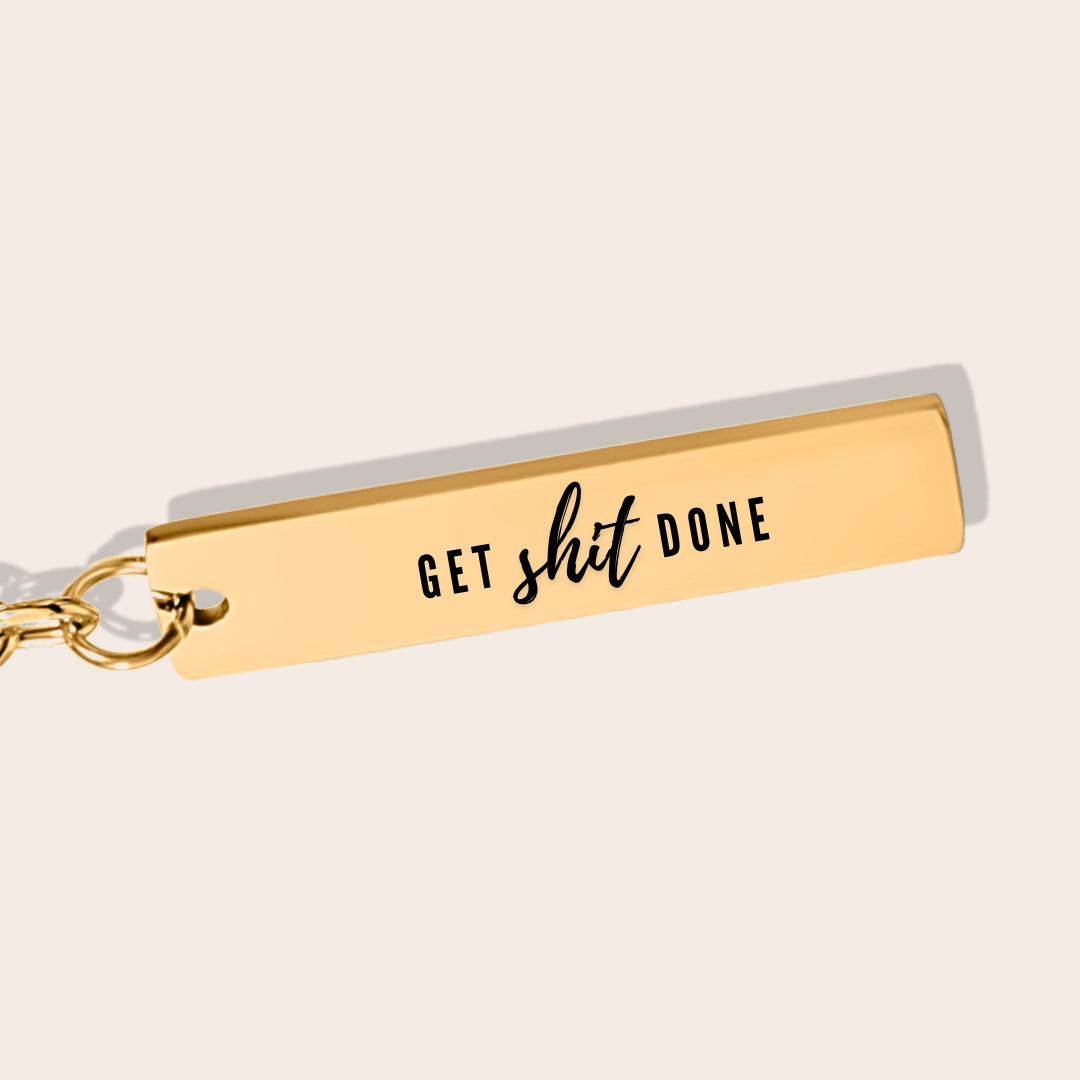 Vertical Bar Keychain - Get Shit Done in gold, close up. This sleek stainless steel stunner, dressed in 18K gold plating, boasts a laser-engraved motto.