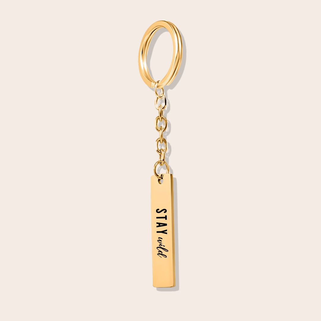 Vertical Bar Keychain - Stay Wild, in gold. Made from durable stainless steel and adorned with 18K gold plating, this sleek piece features a laser-engraved reminder.