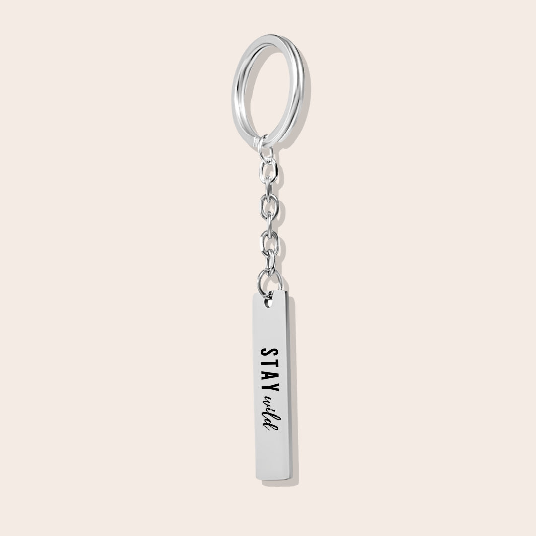 Vertical Bar Keychain - Stay Wild, in silver. Made from durable stainless steel and adorned with 18K gold plating, this sleek piece features a laser-engraved reminder.