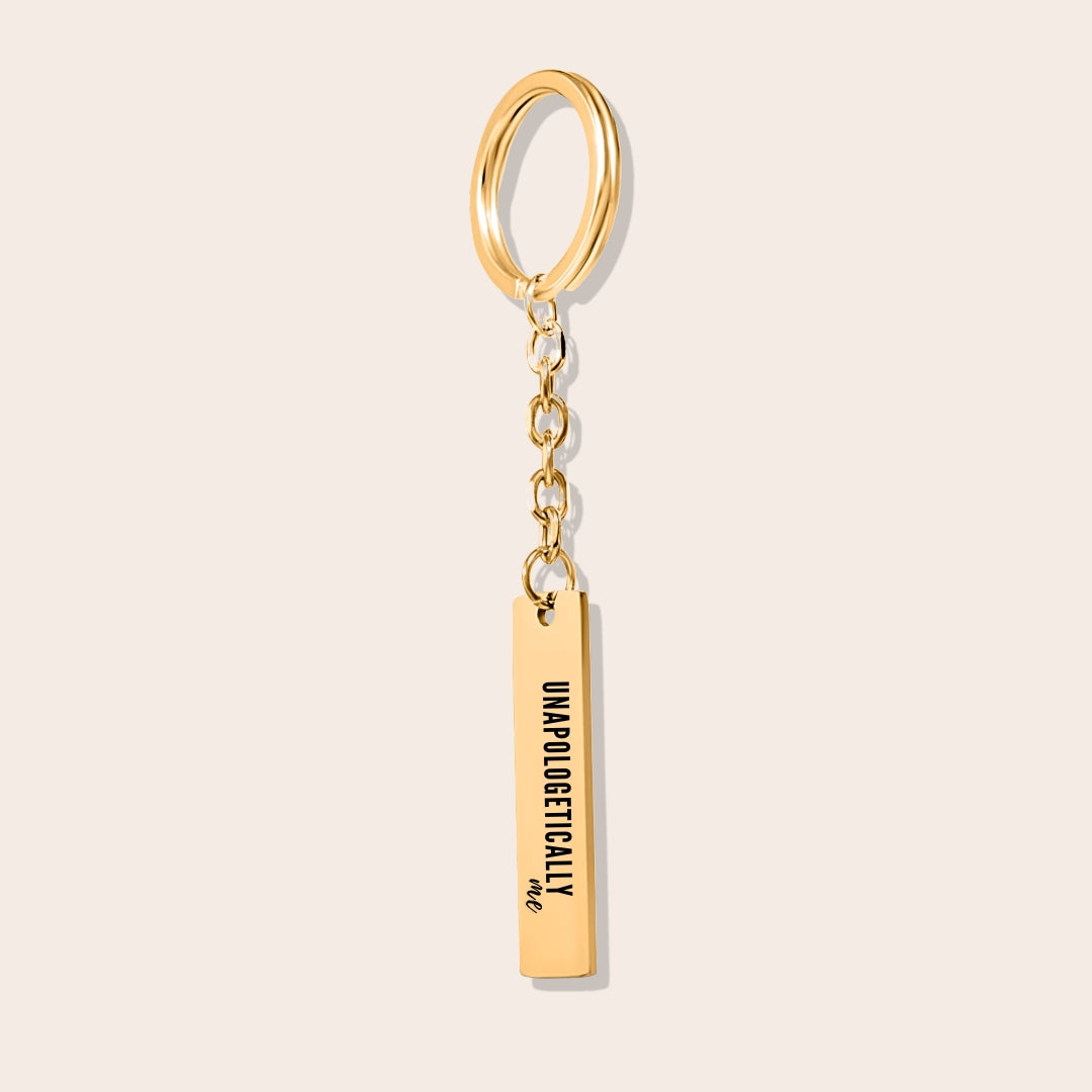 Vertical Bar Keychain - Unapologetically Me, in gold. Created from stainless steel and plated with 18K gold, this sleek piece features a laser-engraved affirmation.