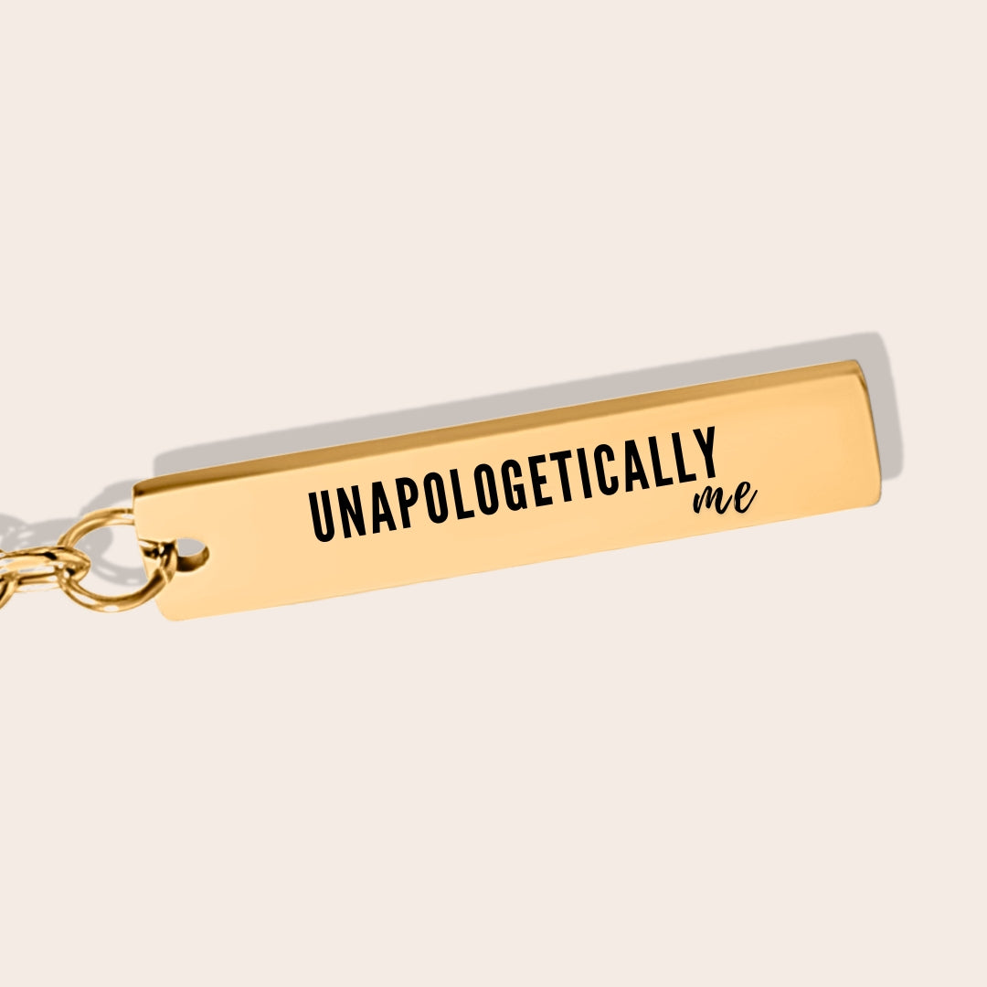 Vertical Bar Keychain - Unapologetically Me, in gold, close up. Created from stainless steel and plated with 18K gold, this sleek piece features a laser-engraved affirmation.