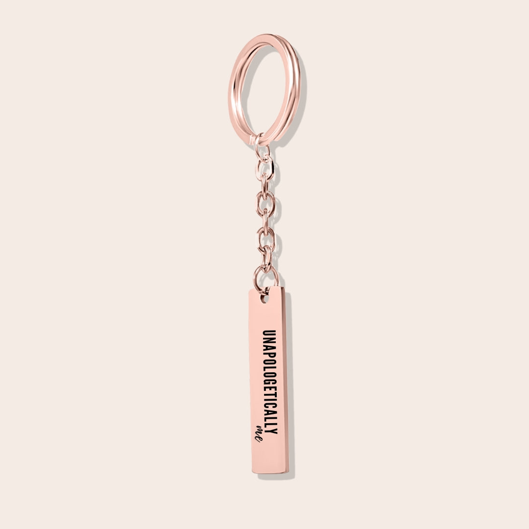 Vertical Bar Keychain - Unapologetically Me, in rose gold. Created from stainless steel and plated with 18K gold, this sleek piece features a laser-engraved affirmation.